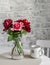 Red roses in a glass vase, tea mug on the table in a cozy room. Beauty home interior still life