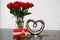 Red roses in glass vase with water and one rose next to vase gift and silver heart