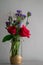 Red roses with purple flowers bouquet in a clear glass jar.