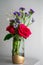 Red roses with purple flowers bouquet in a clear glass jar.