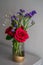 Red roses with purple flowers bouquet in a clear glass jar.