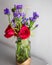 Red roses with purple flowers bouquet in a clear glass jar.