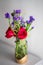 Red roses with purple flowers bouquet in a clear glass jar.