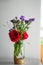 Red roses with purple flowers bouquet in a clear glass jar.