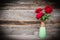 Red roses in vase on wooden background.