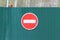 Red round road sign with white stripe prohibiting movement on the green fence of sheet iron. Do not enter. concept of