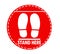 Red round sign with text Stand Here and shoe prints, illustration. Social distancing - protection measure during coronavirus