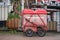 Red royal mail trolley chained to gate with pub garden in background