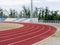 Red running track, colorful grass and empty stands at the stadium, on blue sky. Concept of sport and fitness.