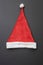Red santa claus hat with white bubo and edging and a pattern in the form of snowflakes on a dark gray background. Top