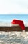 Red Santa\'s hat on wooden bench on the beach