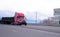 Red semi truck with flat bed trailer transporting industrial car
