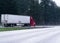 Red semi truck trailer on wide highway with trees