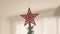 Red shiny sparkling star decoration on the top of a Christmas tree in the sunny home. Close up panned video 4k high