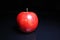 Red shiny whole apple on black reflective studio background. Isolated black shiny mirror mirrored background for every