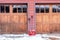 Red shovels on snowy driveway against wall and wooden garage doors of home