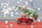 Red small retro toy truck with sparkling bokeh and fireworks delivers Christmas tree on truck body on red and gray background