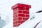 Red smoke brick pipe, chimney close-up, on the roof of a snow-covered house. Symbol of the New Year holidays,