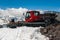 Red snowcat transport on white snow cleans ski track near mountain shelter. Caucasus Mountain