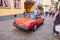 Red sports car drives through town with tourists onlooking.