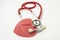 Red stethoscope chestpiece lying to red heart shape on white background vertically isolated. The idea or concept for cardiology -