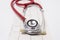 Red stethoscope with chrome details, head in front, lies vertically on three-linear electrocardiogram on white background. Concept