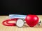 Red stethoscope and red heart in focus, blue medical face mask out of focus on bamboo surface. Dark color copy space. Simple