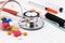 Red stethoscope, syringes, pen, and many colorful pills on blank notepad