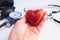 Red stone heart held in hand, stethoscope and pressure meter on white background