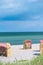 Red striped roofed chairs on empty sandy beach in Travemunde. Grass bush in foreground. Germany