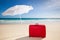 Red suitcase under a white sunshade