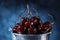 Red sweet cherries close up in a metal bucket on a dark and blue background. Summer taste.