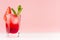 Red sweet cold party drink in elegant shot glass with ice cubes, strawberry slice, green mint on pastel soft pink color background