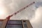 Red tall crane over a newly constructed building. Cloudy sky background. Developing commercial and residential property.