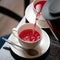 Red tea from frozen berries. Hot drink pouring from teapot into white cup and saucer on wooden table. Tea time. Close up