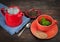 Red teapot with orange teacup and cookies placed on saucer.