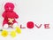 Red teddy bear sit hold the red heart with LOVE lettering made of red seeds and red box of the ring with flowers on white backgrou