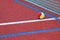 Red tennis court with tennis ball, artificial cover.