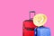 Red textile suitcase & blue hard shell luggage with straw hat hanging on extended telescopic handle, bright solid pink wall backgr
