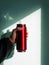 Red thermo can bottle in male hands against wall with harsh shadow.Hot tea coffee drinking in cold autumn winter weather