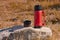 Red thermos with a cup on a stone in the forest on the lawn