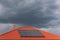 Red tile roof with photovoltaic panels during stormy weather . Solar PV installation and dark blue threatening sky