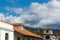 Red tile roof and white Spanish style buildings beneath palm trees, mountains, and fluffy clouds in Santa Barbara, California