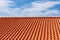 Red tiles panels roof under blue sky.