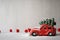 Red toy car with a Christmas tree on the roof in the snow, on a gray background with red New Year`s toys. Place for text