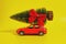 Red toy car with Christmas tree on the roof on yellow background
