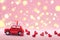 Red toy car delivering carrying on roof gift box with small red hearts on pink background. Valentine`s day concept