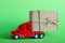 Red toy car truck delivers a parcel in a craft cardboard box on green background. Delivery, gifts or donation concept