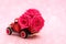 Red toy truck delivering bouquet of rose flowers on pink background with bokeh. February 14, Valentine`s day, 8 March,