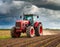 Red tractor drives across a vast field under a dramatic stormy sky. Generated with AI